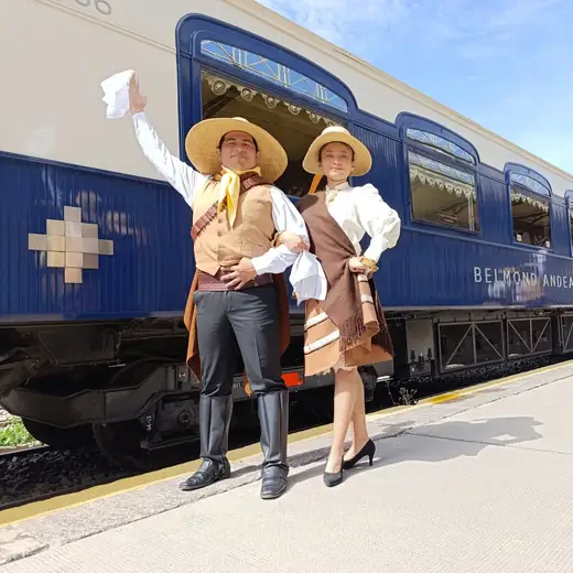 Pareja de bailarines con sombrero y vestuario tradicional junto a un tren azul en una estación