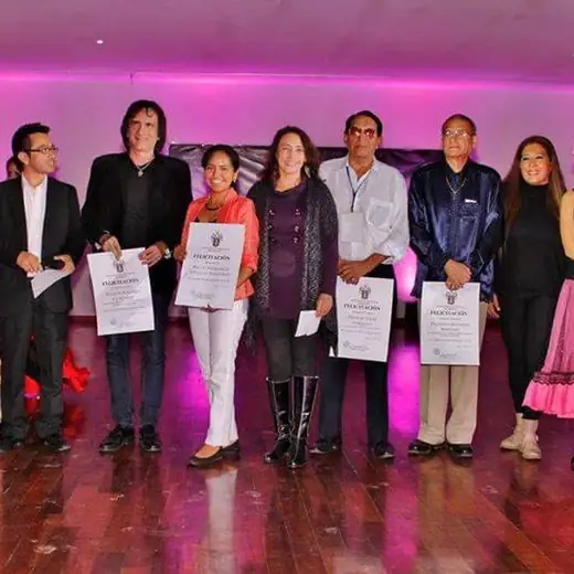 Participantes de una ceremonia con diplomas, junto a bailarinas con vestuario típico