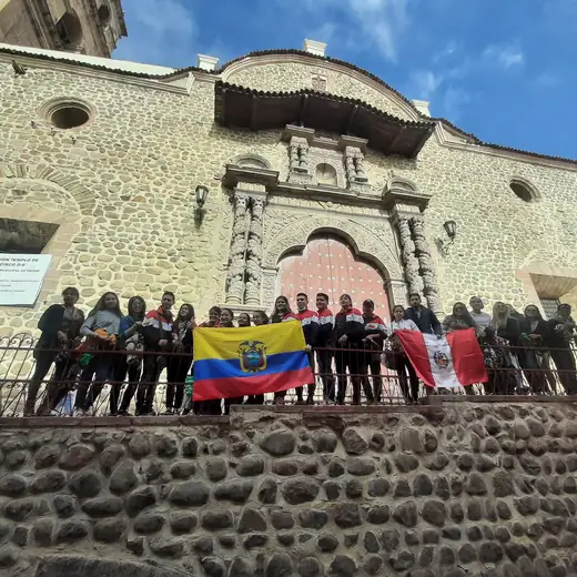 Grupo de participantes con las banderas de Ecuador y Perú frente a una iglesia de piedra