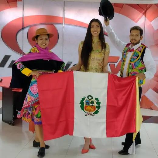 Tres integrantes del elenco con vestuario andino y la bandera del Perú en un set de televisión