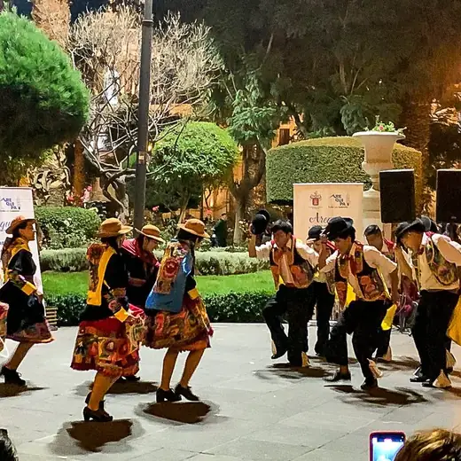Danza andina de noche en una plaza, con público alrededor