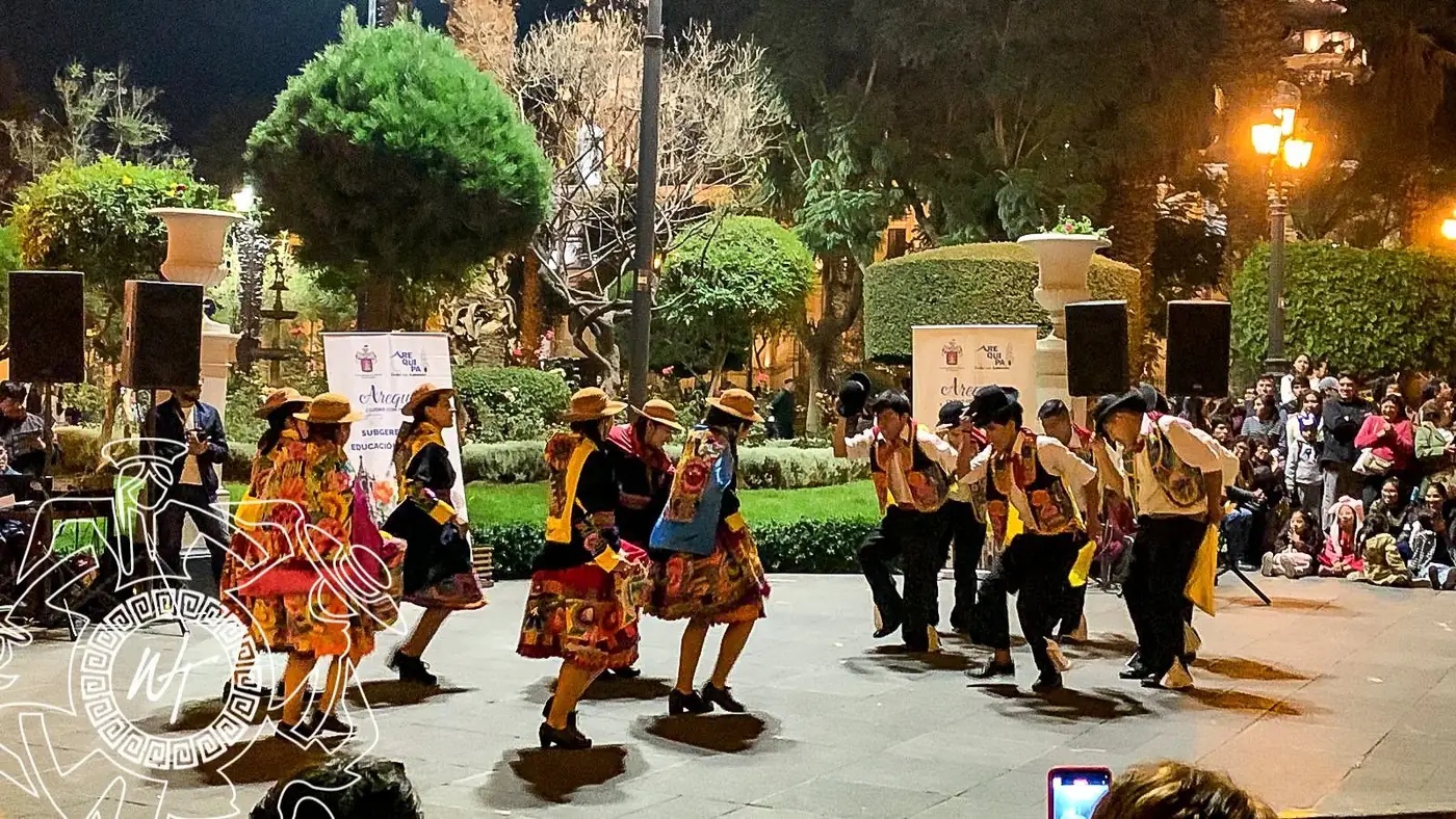 Danza andina de noche en una plaza, con público alrededor