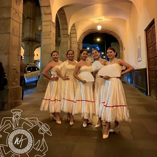 Bailarinas con vestidos blancos bajo los arcos iluminados de un portal