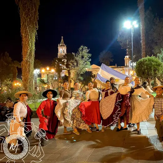 Bailarines con trajes de estilo gaucho y faldas rojas en una plaza de noche