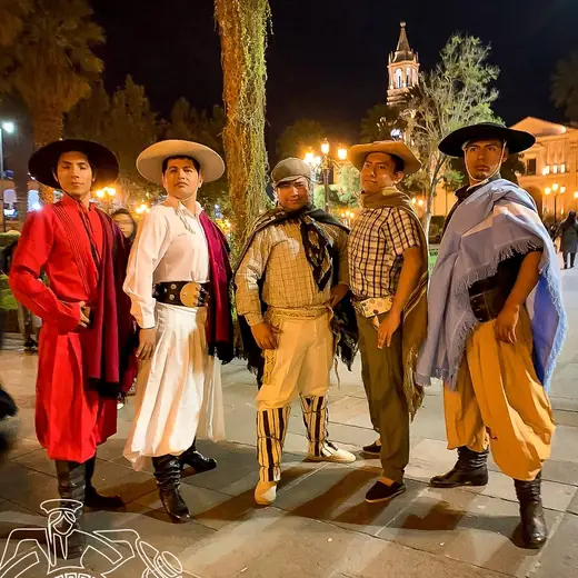 Cinco bailarines con vestuario de gaucho posando en una plaza de noche