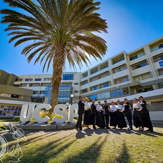 Elenco con vestuario negro frente a un edificio universitario y una palmera