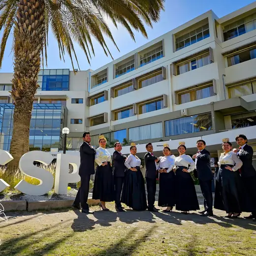 Elenco posando frente al letrero de una universidad, con una palmera detrás