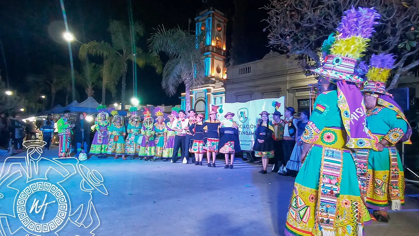 Comparsa con trajes coloridos y un gran tocado en una fiesta nocturna