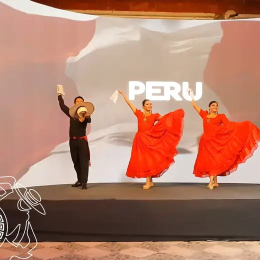 Bailarines con vestidos naranjas en un escenario con el letrero PERU