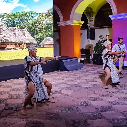 Bailarín con poncho sobre un escenario con casas de paja de fondo