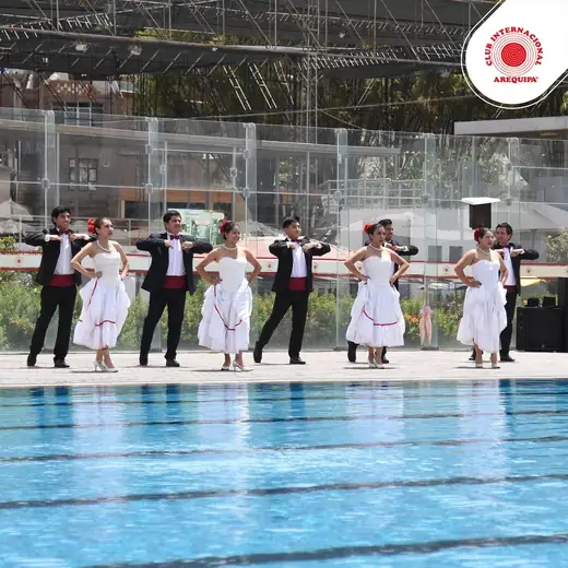 Parejas de baile con vestidos blancos y trajes oscuros junto a una piscina