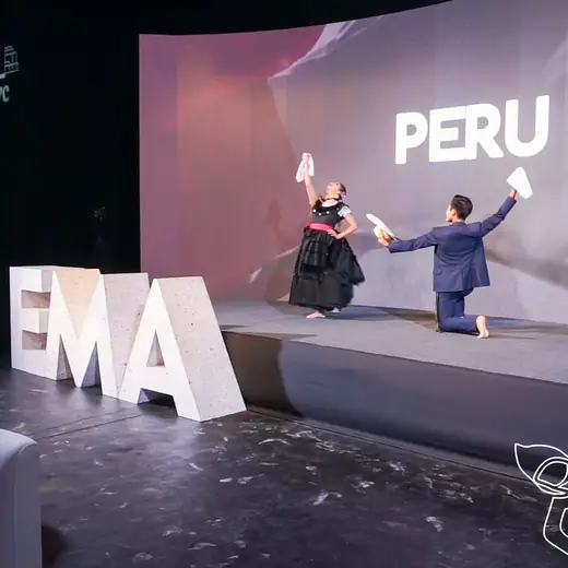 Pareja de bailarines en un escenario con el letrero PERU