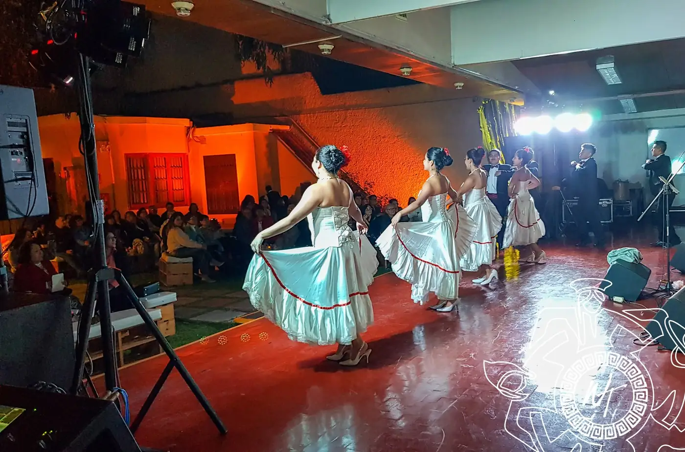 Bailarinas con vestidos claros girando sobre un piso rojo ante el público