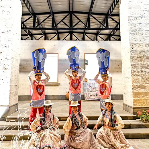 Tres bailarines con tocados azules y polleras posando en un patio de piedra