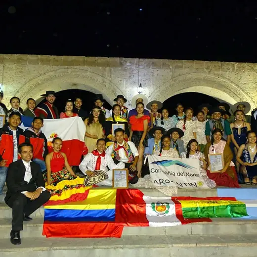 Grupo grande con banderas de varios países posando de noche frente a unos arcos